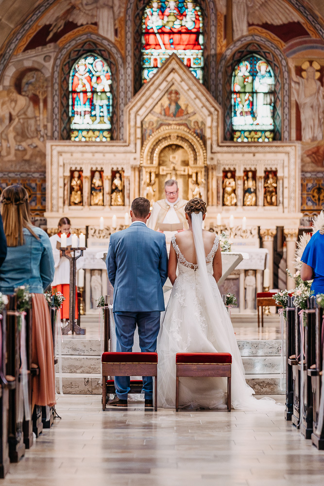 Foto von Lisa Werner Fotografie, Hochzeit, Brautpaar bei kirchlicher Trauung, Mittelgang mit Blick auf das Brautpaar